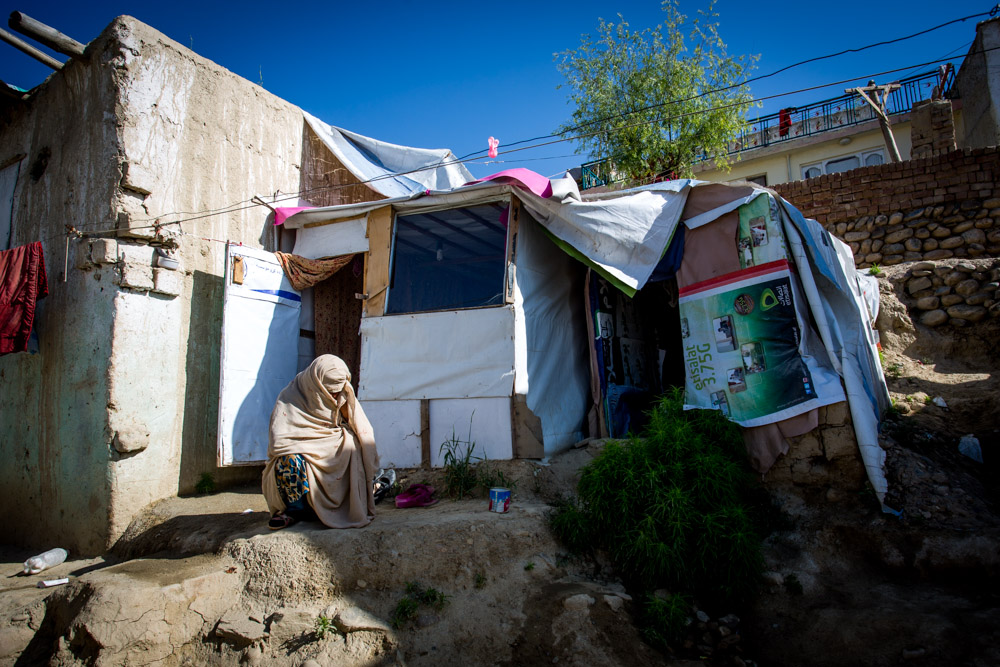 A widow crouches outside of her tiny, makeshift home