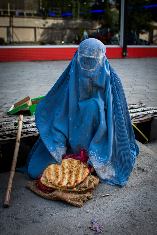A widow begs on a busy road in Kabul; the two loaves of bread she now has are the dinner for her family of eight.